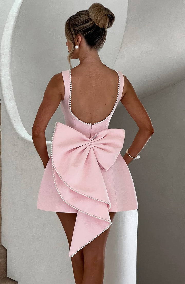 Model wearing a sophisticated women's bow-back mini party dress. Ideal for summer cocktails & special occasions.