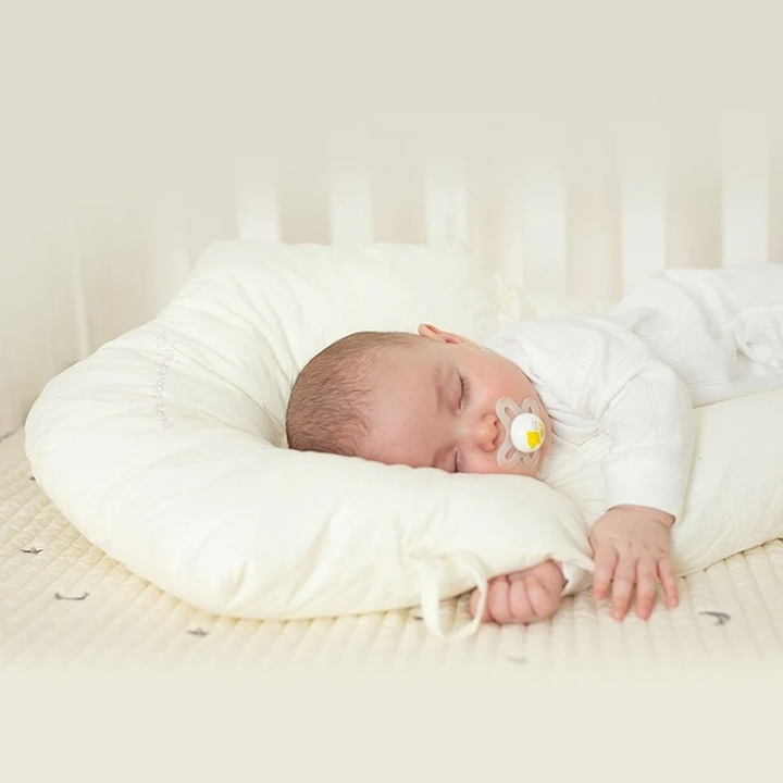 Infant sleeping peacefully on a white hypoallergenic baby sleep pillow, ensuring safe & gentle head and neck support.