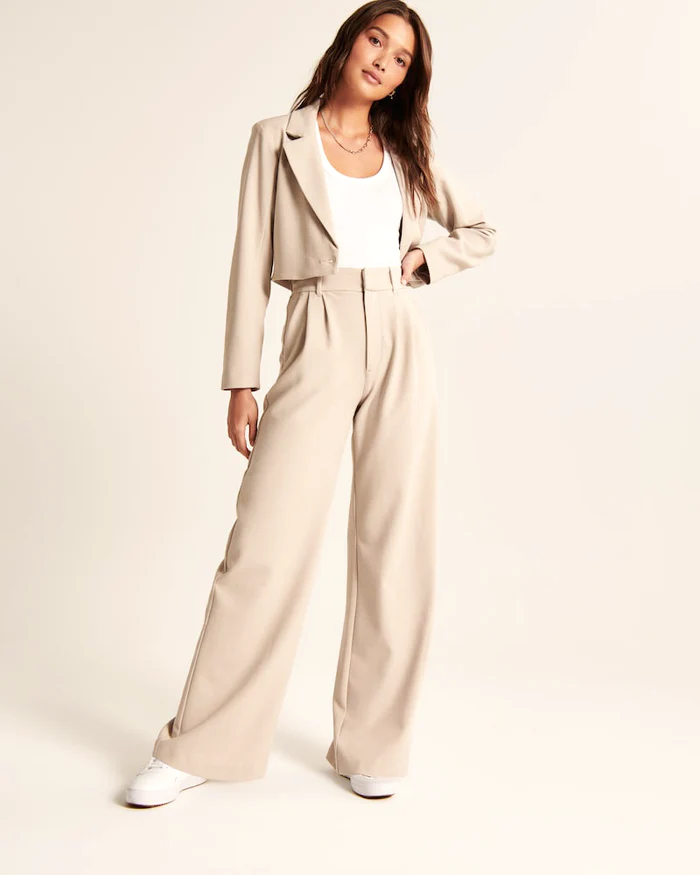 Model wearing women's beige wide-leg tailored trousers, high-waist, elegant style for both formal and casual occasions.
