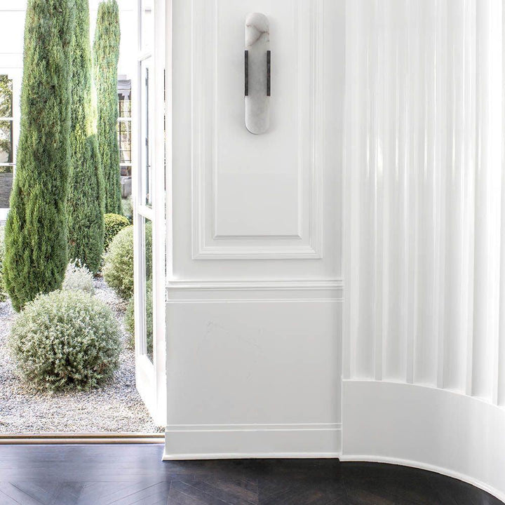 "Modern elongated alabaster wall lamp with metal and brass accents, emits warm glow, suitable for chic interior decor."