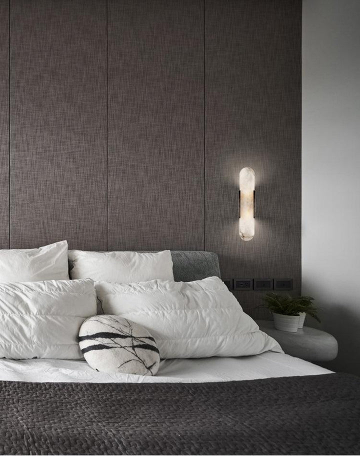 "Modern elongated alabaster wall lamp with metal and brass accents, emits warm glow, suitable for chic interior decor."