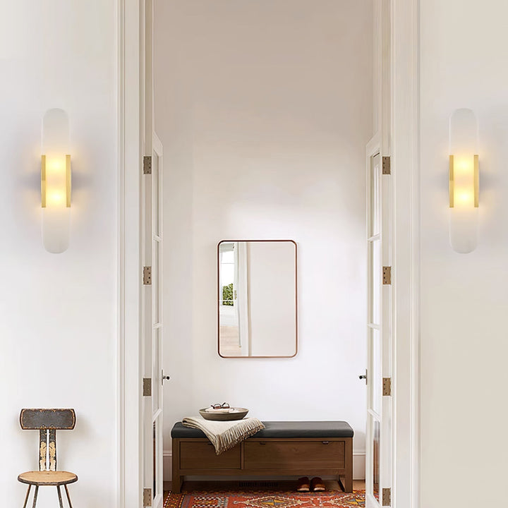 "Modern elongated alabaster wall lamp with metal and brass accents, emits warm glow, suitable for chic interior decor."