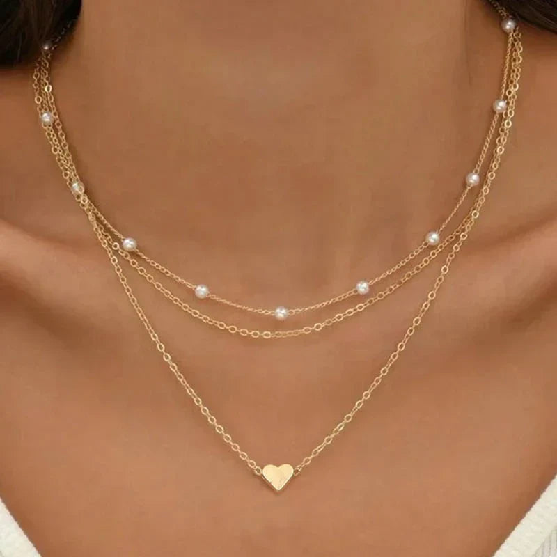 Women's 3-layered gold necklace with delicate chains, heart or cross pendant, and a faux pearl accent.