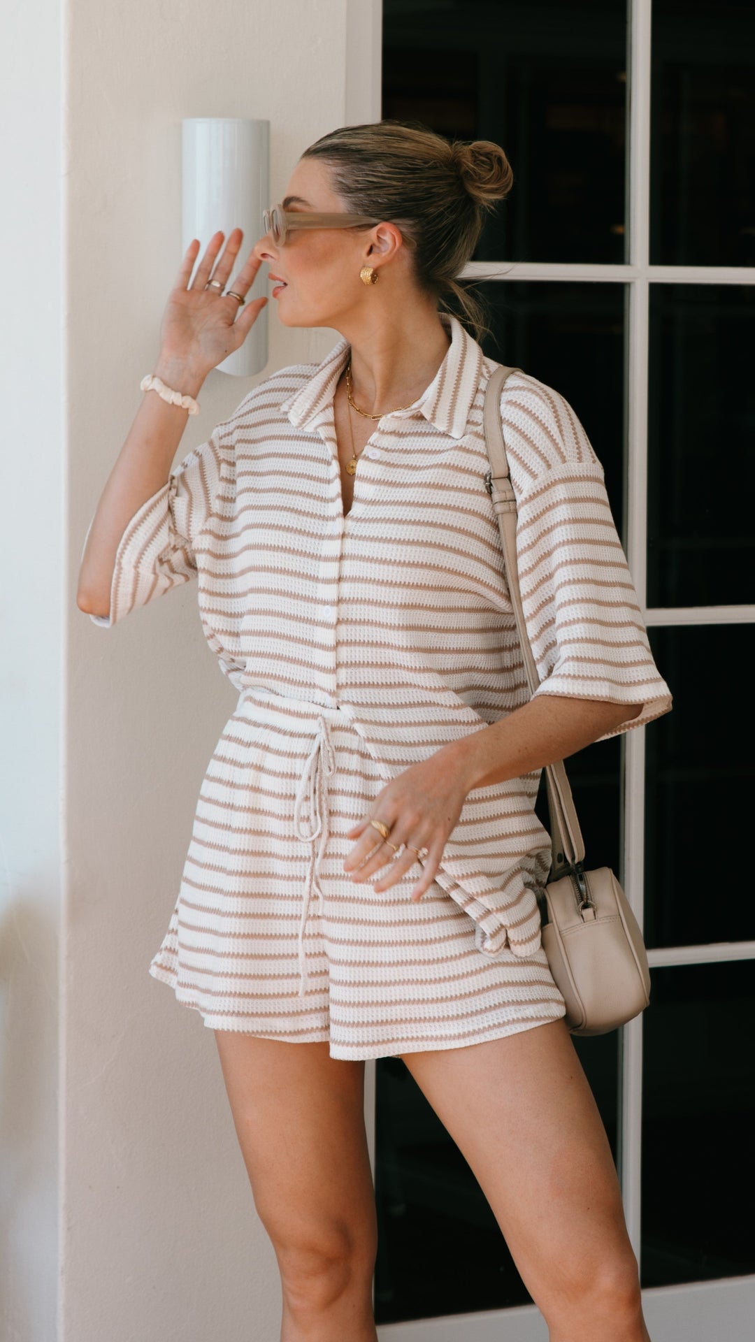 Stylish women's beige and white striped button-up shirt, part of a chic summer shorts set. Vacation wear.