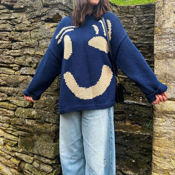 Women's oversized smiley face sweater styled with jeans. A trendy, cozy knit top for casual fall fashion and warmth.