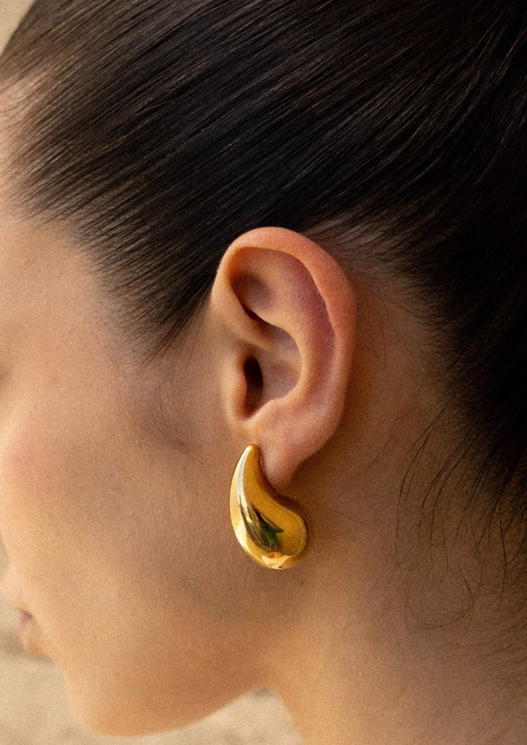 Woman showcasing beautiful polished teardrop dangle earrings. Chic and fashionable jewelry.